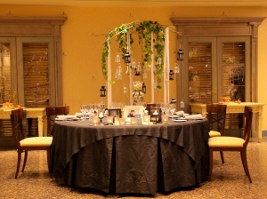 Composición de mesa con cubre mantel y faldón gris con sillas en cerezo barnizado y asiento acolchado color vainilla envuelto en luz cálida vista plano general